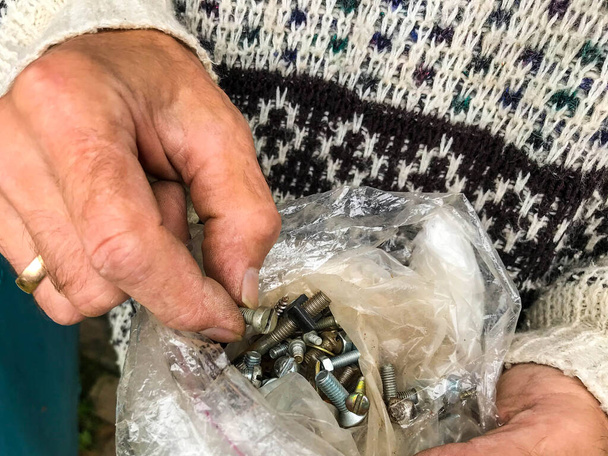 the man is holding a plastic bag with various repair tools. a man goes through nails, nuts, bolts. the man is wearing a knitted gray sweater, DIY repair - Photo, Image