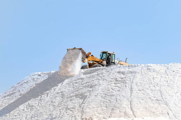 Huelva, España - 1 de octubre de 2020: Excavadora trabajando en una enorme pila de sal en salinas en Marismas del Odiel. Sal marina producida por la evaporación del agua de mar. - Foto, Imagen