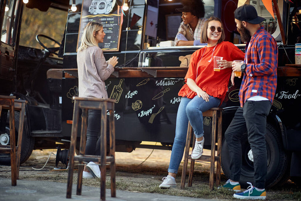 Friends chilling out with beer in front of food truck - Fotó, kép