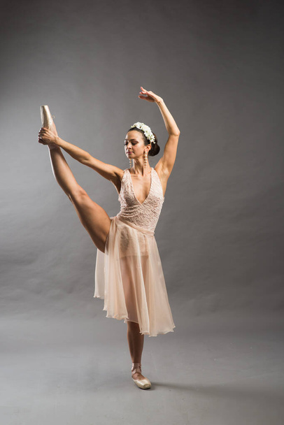 young beautiful ballet dancer in beige swimsuit posing on pointes on light grey studio background - Foto, imagen