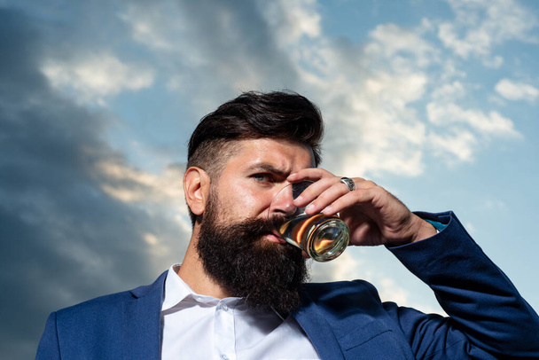 Close up of a stylish handsome bearded man enjoying brandy or whiskey. - Фото, зображення
