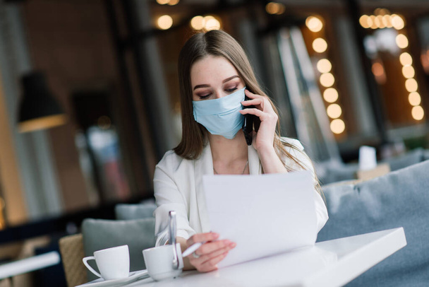 Serious woman with protective face mask looking at smart phone checking news on a cafe - Photo, Image