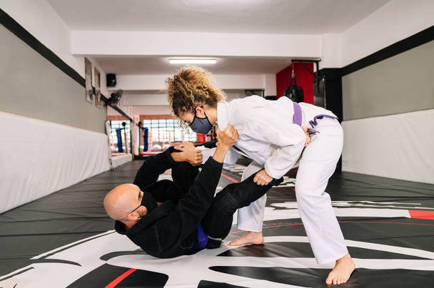 Homem e mulher treinando artes marciais e judô com quimonos no tapete de chão do ginásio com uma máscara facial por causa da pandemia de coronavírus covid 19 - Foto, Imagem