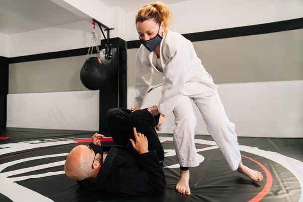 Mężczyzna i kobieta trenują sztuki walki i judo z kimonami na macie gimnastycznej z maską twarzy z powodu pandemii covid 19 - Zdjęcie, obraz