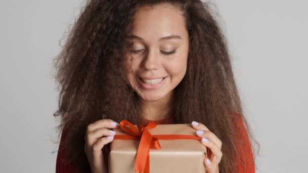 Hermosa chica morena excitada recibe regalo en su cumpleaños mirando felizmente en cámara aislada sobre fondo blanco - Metraje, vídeo