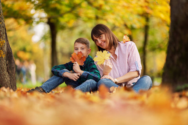 Mom and son are sitting on the ground in a beautiful autumn forest. Love and tenderness. - Foto, Bild