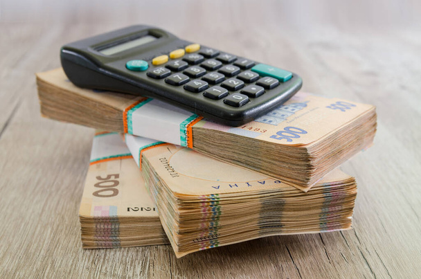 Három köteg hrivnya és egy számológép egy fából készült asztalon. Ukrán pénz. 500 hrivnya bankjegy. Egy csomó ukrán pénz.. - Fotó, kép