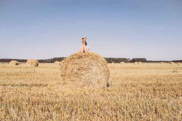 Girl relaxing on hay bale in summer field. Harvesting, end of summer. Countryside slow life. - Fotó, kép
