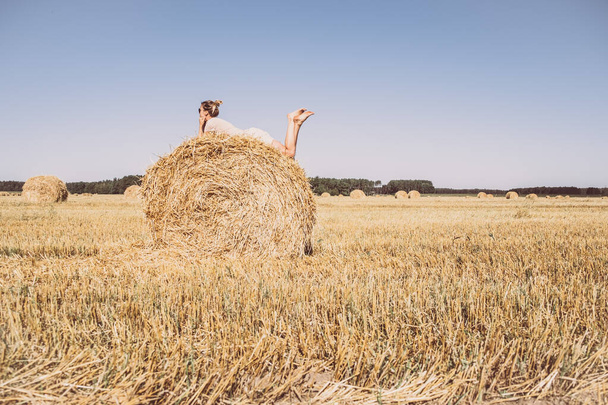 女の子は干し草の上で凍る。農場で夏。空に対するフィールド上のヘイバレス。スペースのコピー. - 写真・画像