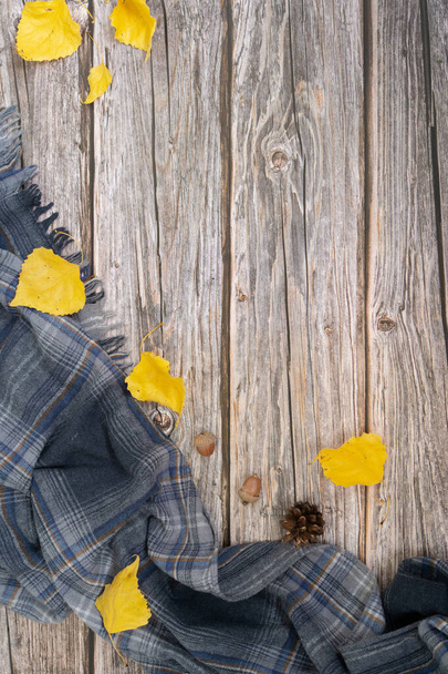 Autumn flat lay with gray scarf and dry leaves of yellow color on wood background.  - Фото, зображення