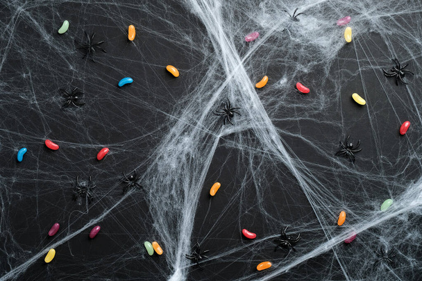 Happy halloween holiday concept. Colorful halloween candies and spiderweb on black background. Flat lay, top view. - Foto, Imagem
