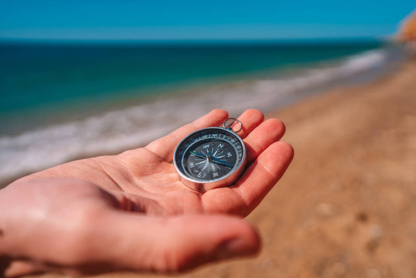 Mano sosteniendo una brújula con vista a la arena y al mar - Foto, imagen