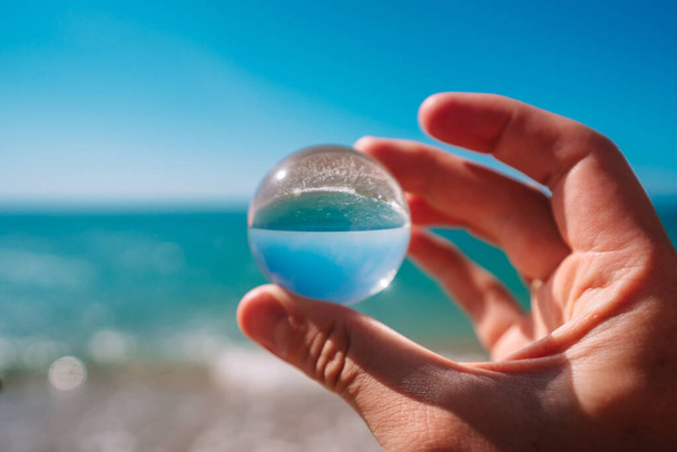 円形のクリスタルボールを通して海の写真は、ボールの写真を上下に回転させます。ボールの中の写真は焦点が合っており、背景は焦点が合っていません. - 写真・画像