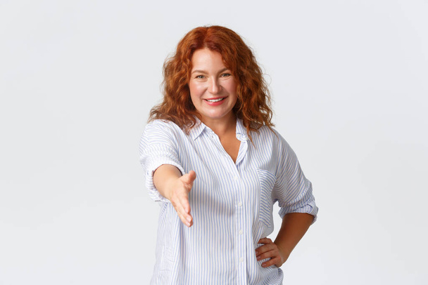 Confident smiling middle-aged redhead female entrepreneur, businesswoman extend hand for handshake, greeting business partner, introduce herself like professional, white background - Photo, image