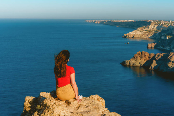Zadní pohled na cestovatelku stojící na okraji útesu před úžasným mořským pláštěm. Svoboda, cestování a dovolená. - Fotografie, Obrázek