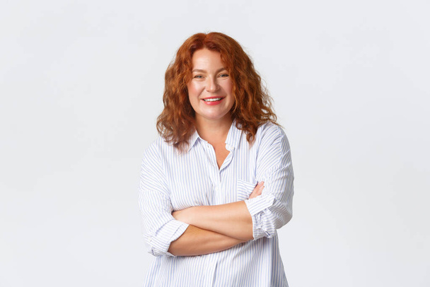 Smiling upbeat redhead middle-aged woman, feeling like professional, cross arms chest and looking confident at camera. Adult female starting own business, standing white background - Photo, image