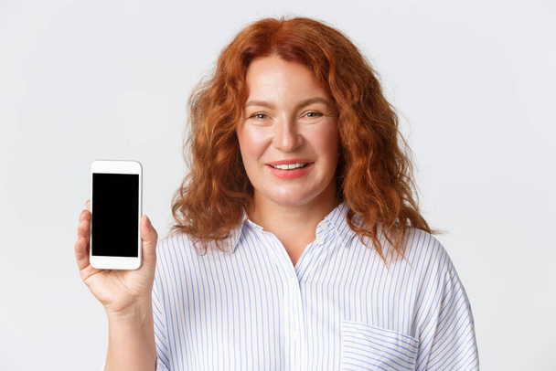 People, emotions and technology concept. Close-up of pleased pretty middle-aged woman, showing smartphone screen and smiling, recommend mobile application or cellular service - Fotoğraf, Görsel