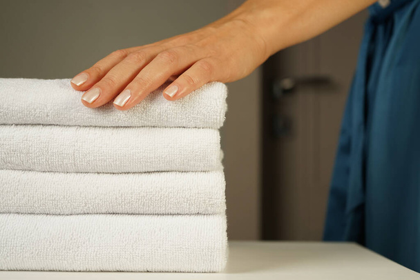 woman in a turquoise silk robe with beautiful hands with a good manicure holds a neatly folded pile of white terry towels indoors - Photo, image
