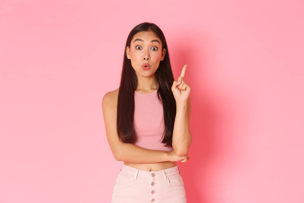 Lifestyle, beauty and women concept. Creative attractive asian girl in summer clothes have solution, raising index finger and saying her idea, think up great plan, standing pink background - Photo, Image