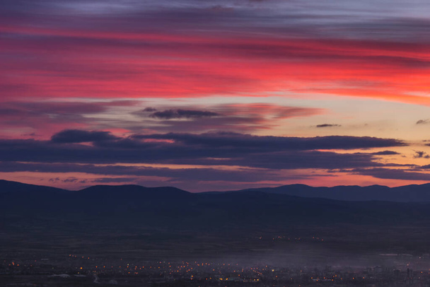 Dramatyczny, kolorowy zachód słońca nad odległym miastem pokrytym mgłą i górami horyzontu sylwetki - Zdjęcie, obraz