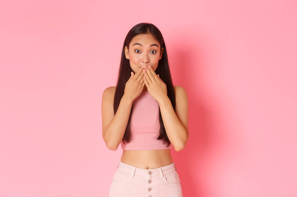 Lifestyle, beauty and women concept. Close-up of amused and surprised pretty, silly asian girl cover mouth with palms and looking coquettish while gossiping, found out secret, pink background - Photo, Image