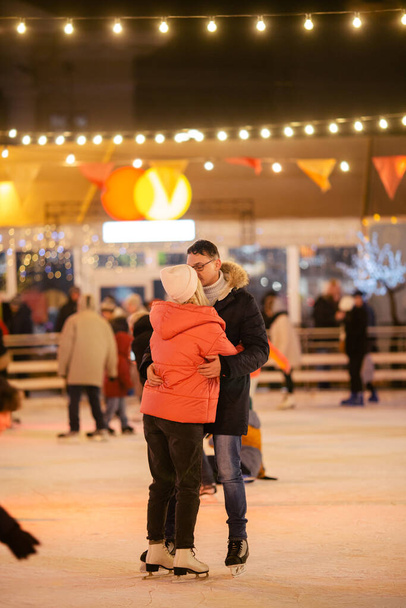 Beautiful couple have fun in ice arena. active date ice skating on ice arena in evening city square in winter Christmas Eve. St. Valentine's Day at the city ice rink. New Year's holidays in city Kiev. - 写真・画像