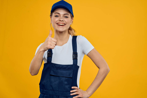 Mujer en uniforme de trabajo gorra azul entrega servicio de mensajería fondo amarillo - Foto, Imagen