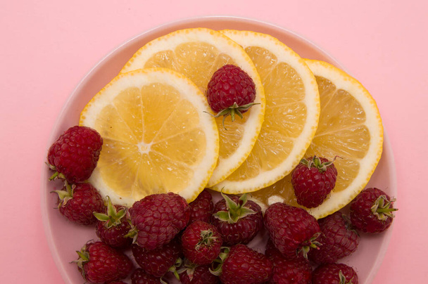 lemon slices and raspberries in a pink plate on a pink background. Flat lay of tropical summer. Nutrition concept.Disease prevention - Photo, Image