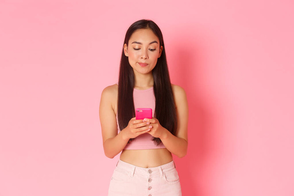 Teknologia, viestintä ja online-elämäntapa käsite. Huomaavainen kaunis aasialainen nainen etsii epämääräinen matkapuhelimen näytöllä miettiessään mitä ostaa, ostoksia internetissä älypuhelimen sovellus - Valokuva, kuva