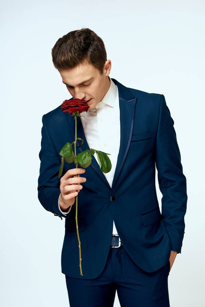 Un homme en costume avec une rose dans ses mains un cadeau date fond clair - Photo, image