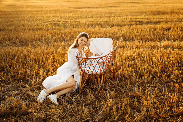 Elegant woman near tiny bed with beautiful newborn baby girl at the field, loving mother take care of little daughter, tender family moments, parenting and maternity concept - Valokuva, kuva