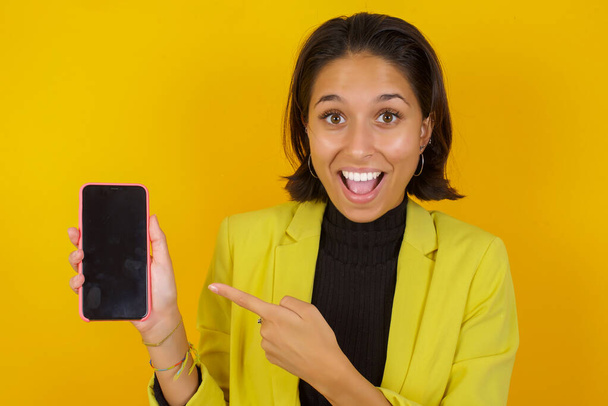 bella giovane donna con smartphone posa contro muro giallo, stusio colpo - Foto, immagini