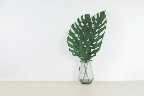 木のテーブルの上のガラス花瓶の熱帯の葉,フロントビュー,テキストのためのスペース. - 写真・画像