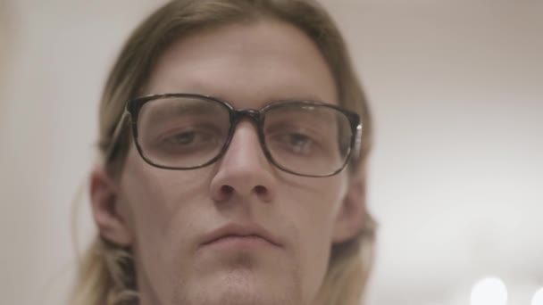 Young man with downcast eyes. Stock. Close-up of young man with glasses with drooping look and tired look. Hipster in glasses with indifferent drooping look - Footage, Video