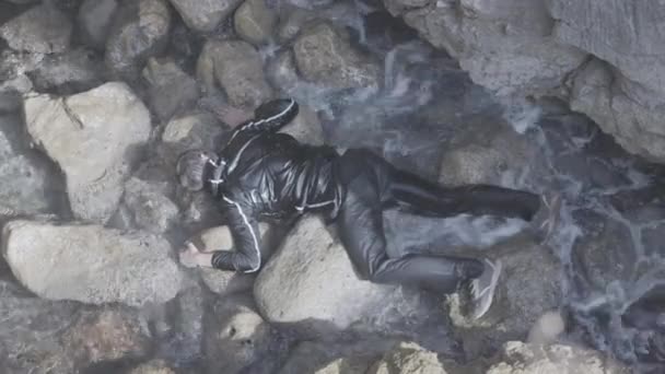 石の上で死んだ男。株だ。波と岩の上に横になっている男の死体の上からの眺め。死んだ男は海によって岩に運ばれた。死体、事故、殺人 - 映像、動画