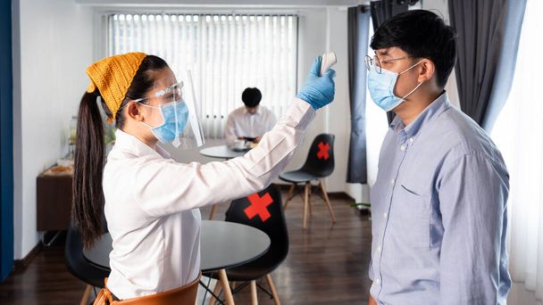 kelnerka nosząca maskę i sprawdzająca temperaturę ciała klienta przez czujnik wykorzystuje medyczny termometr na podczerwień cyfrową przed wejściem do restauracji dla ochrony przed koronawirusem (COVID-19). - Zdjęcie, obraz