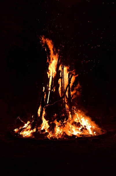 Isoliertes Bild eines Lagerfeuers mit Flammenflecken, die in der Dunkelheit in der Luft wehen - Foto, Bild