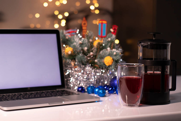Fransız presinin yanında beyaz ekranlı dizüstü bilgisayar ve yeni yıl dekorasyonlarına yakın çay. Noel tema şablonu - Fotoğraf, Görsel