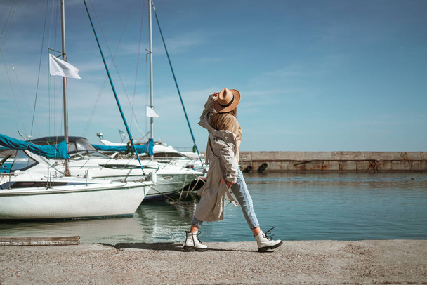 Egy lány bézs ballonkabátban és kalapban sétál a jacht klubban. - Fotó, kép