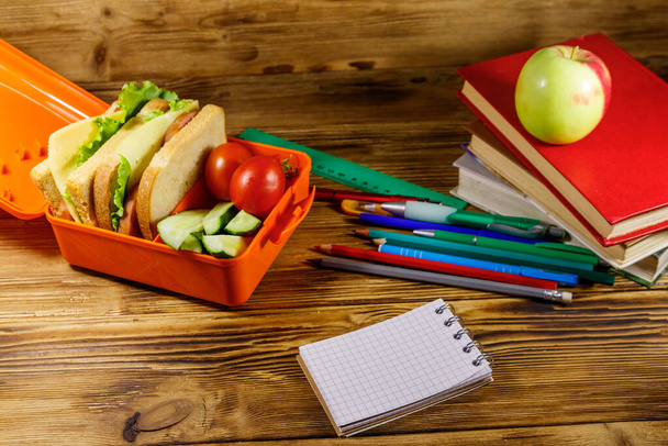 Wracając do koncepcji szkoły. Przedmioty szkolne, książki, jabłko i pudełko na lunch z kanapkami i świeżymi warzywami na drewnianym biurku - Zdjęcie, obraz