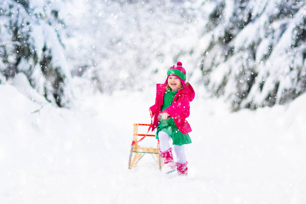 Little girl enjoying a sleigh ride. Child sledding. Toddler kid riding a sledge. Children play outdoors in snow. Kids sled in the Alps mountains in winter. Outdoor fun for family Christmas vacation. - Photo, Image