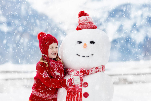 Děcko buduje sněhuláka. Děti stavějí sněhuláka. Chlapec a dívka si hrají venku na sněžný zimní den. Venkovní rodinná zábava na vánoční dovolenou v horách. Děti si hrají ve Švýcarské horské krajině. - Fotografie, Obrázek
