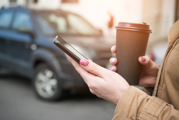 woman hands with mobile phone and big coffee cup on city street - Photo, Image