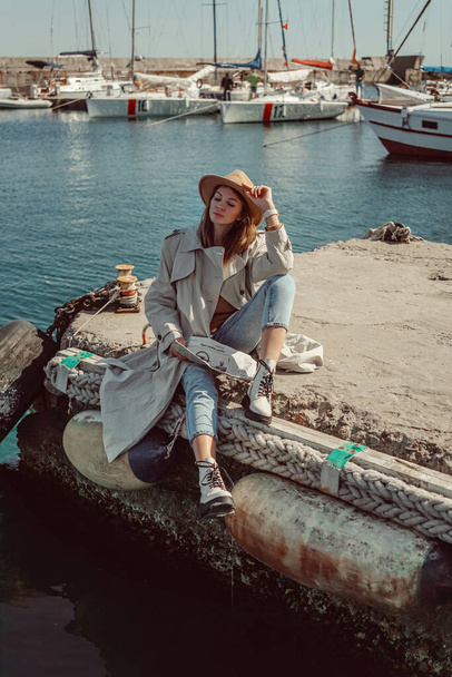a girl in white shoes and a hat sits on a pier in a yacht club, reads a newspaper and has a rest. new collection of footwear autumn winter 20/21 fashion photo Lubeck, Germany september 2020 - Photo, Image