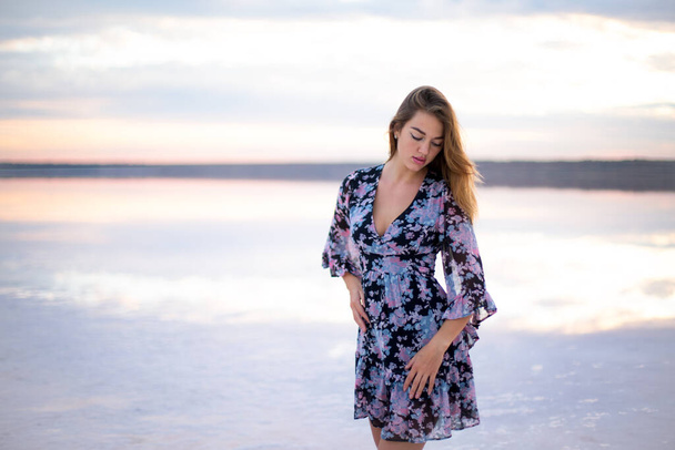 belle fille dans une robe de fleur sur un lac rose salé à un coucher de soleil vanille - Photo, image