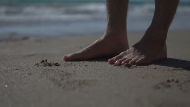 Man wandelen, stappen en staan bij het gouden zand aan zee strand. Superslow motion. Lage hoek op de foto op mannelijke benen lopen in de buurt van de oceaan. Barefoot Op zandstrand met golven. Zomerkust. - Video