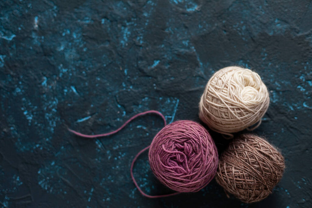 tres bolas de color marrón rosado beige madeja de hilo de lana para ganchillo y tejer en hormigón masilla textura azul oscuro. Imagen plana con espacio para texto. - Foto, Imagen