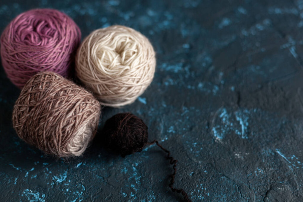 Cuatro bolas de color marrón rosado beige madeja de hilo de lana para ganchillo y tejer en hormigón masilla textura azul oscuro. Imagen plana con espacio para texto. - Foto, Imagen