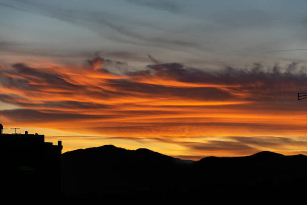 крупним планом вогненні кольорові хмари під час тропічного заходу сонця з силуетом гірського хребта нижче
 - Фото, зображення
