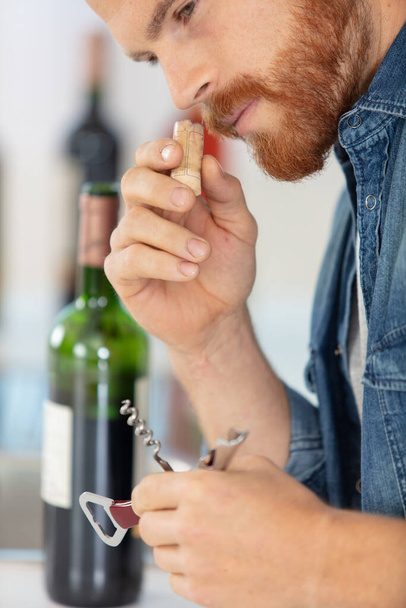 young man standing at the table and opening red wine - Photo, image